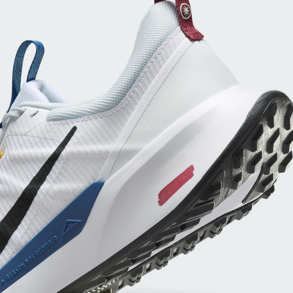 Highlights the "unreal" clean finish where the white foam midsole meets the blue trail clip, painted red trail signpost graphic, and toothy black rubber tread below.