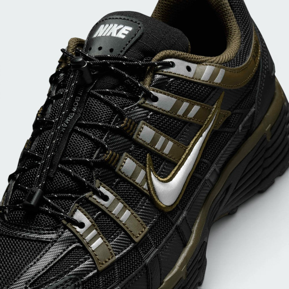 Details the micro-precision of the black mesh toe box, showing the silver metallic Swoosh, reflective eyelet strips, toggle lace lock, and "NIKE" block lettering on the tongue tag.