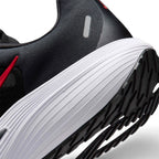 Close-up of a black athletic shoe showing the side heel area, featuring a thick white ribbed midsole, black outsole, and a small red accent near the collar.