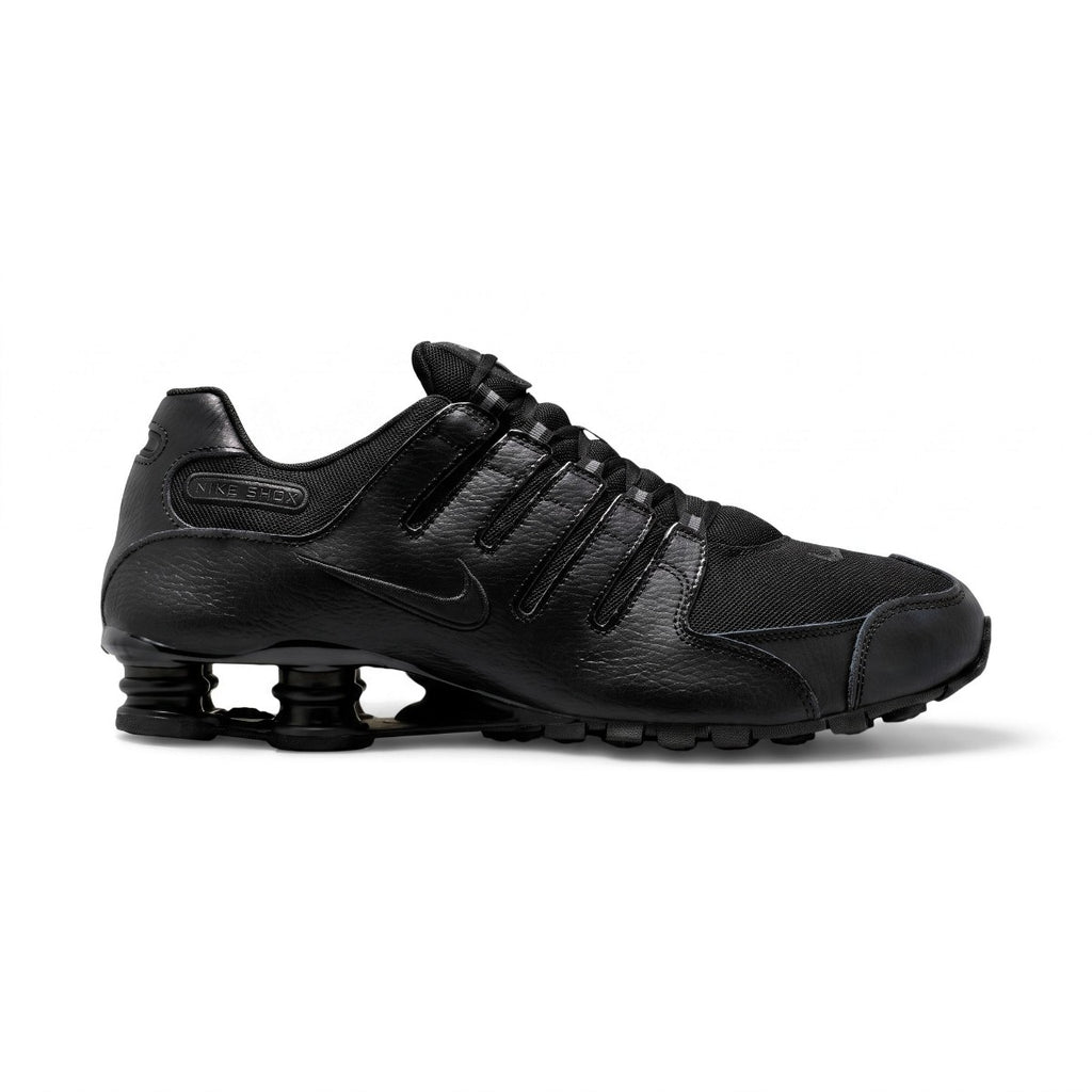 Studio lateral view of the Nike Shox NZ in all black, highlighting the synthetic leather and textile upper, ghillie lacing system, embossed Nike Shox badge, and black Shox cushioning columns in the heel.