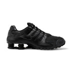 Studio lateral view of the Nike Shox NZ in all black, highlighting the synthetic leather and textile upper, ghillie lacing system, embossed Nike Shox badge, and black Shox cushioning columns in the heel.