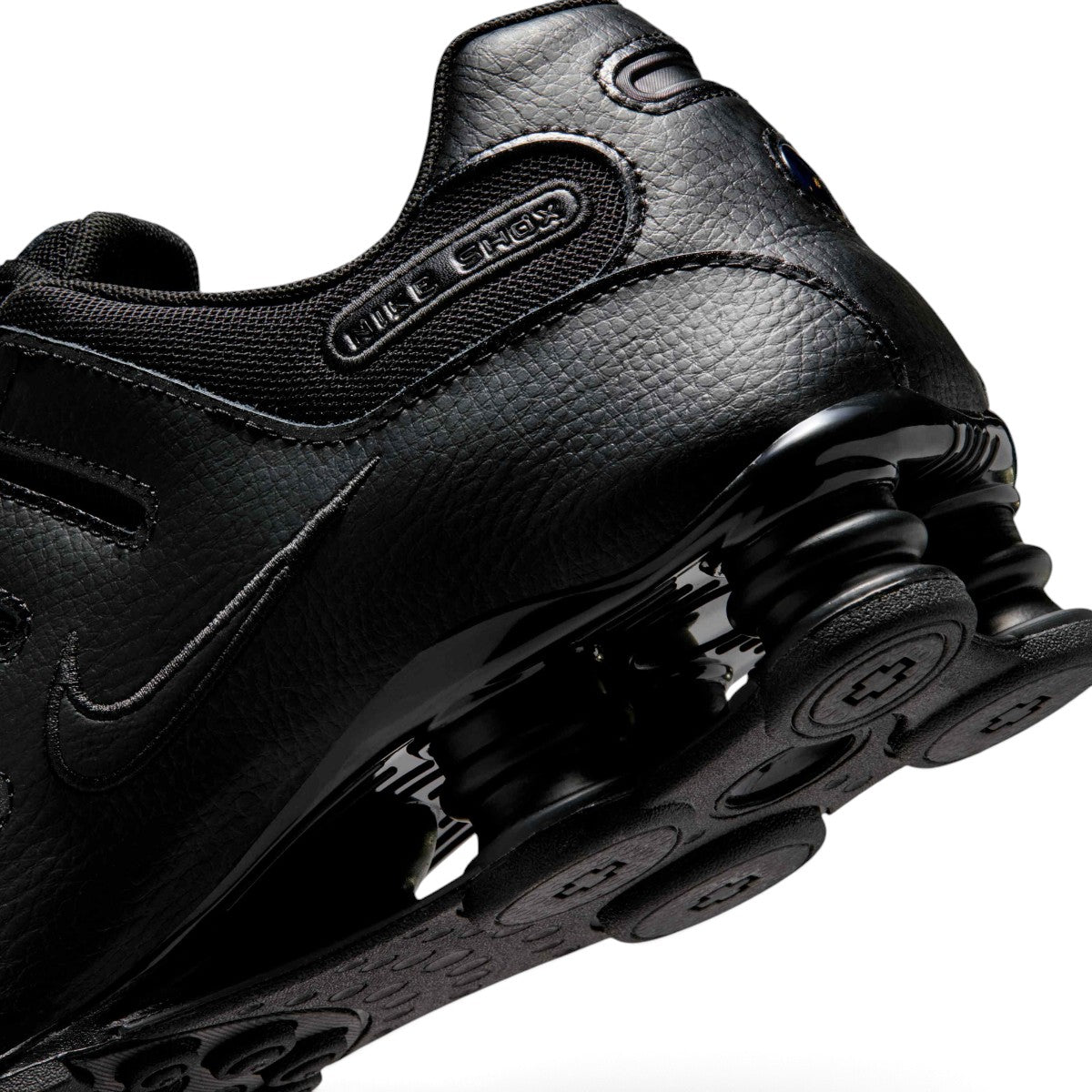 Detailed close-up angle capturing the embossed "NIKE SHOX" quarter branding, smooth leather heel panels, and the glossy finish of the springy Shox cushioning units.