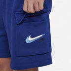 Close-up of a person wearing royal blue Nike cargo shorts, showing a front pocket with a large white and light blue Nike Swoosh logo and a smaller dark Nike wordmark.