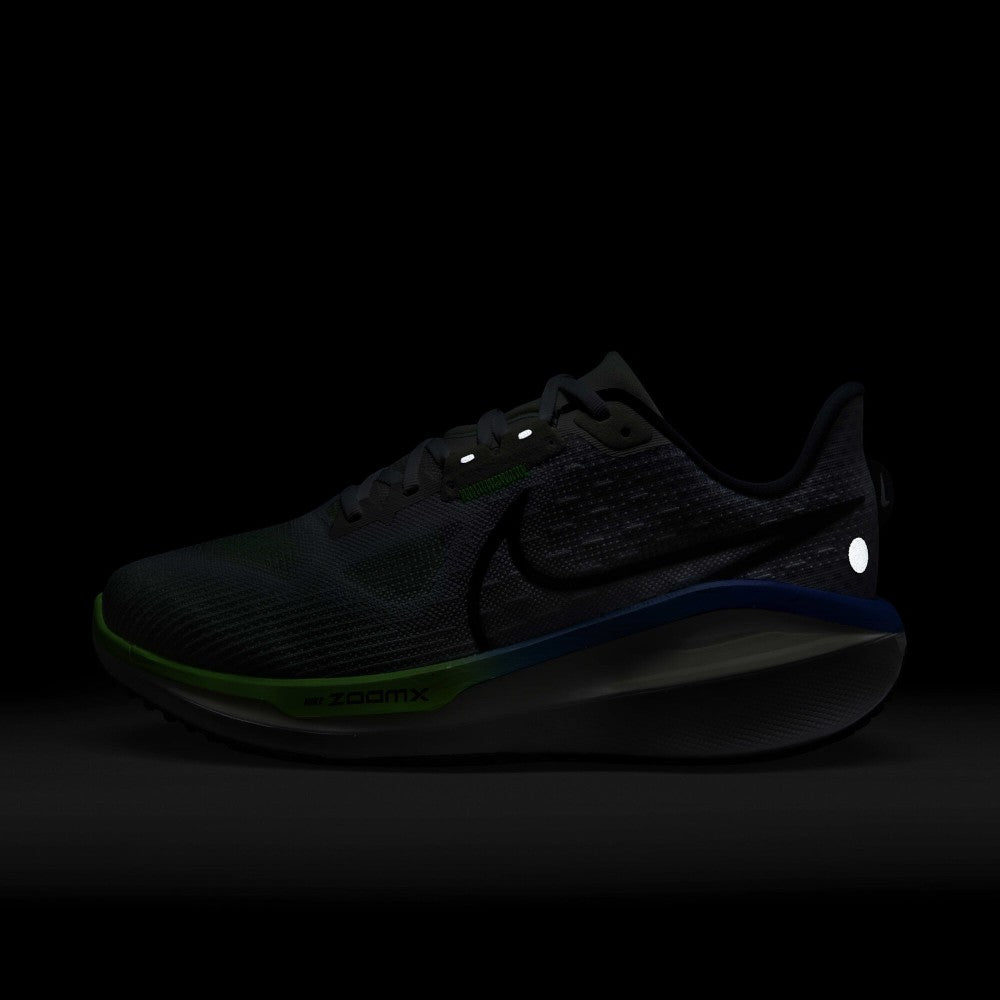 A dark Nike running shoe shown in low-light conditions against a black background, with visible green and blue accents on the midsole and a reflective white dot near the heel.