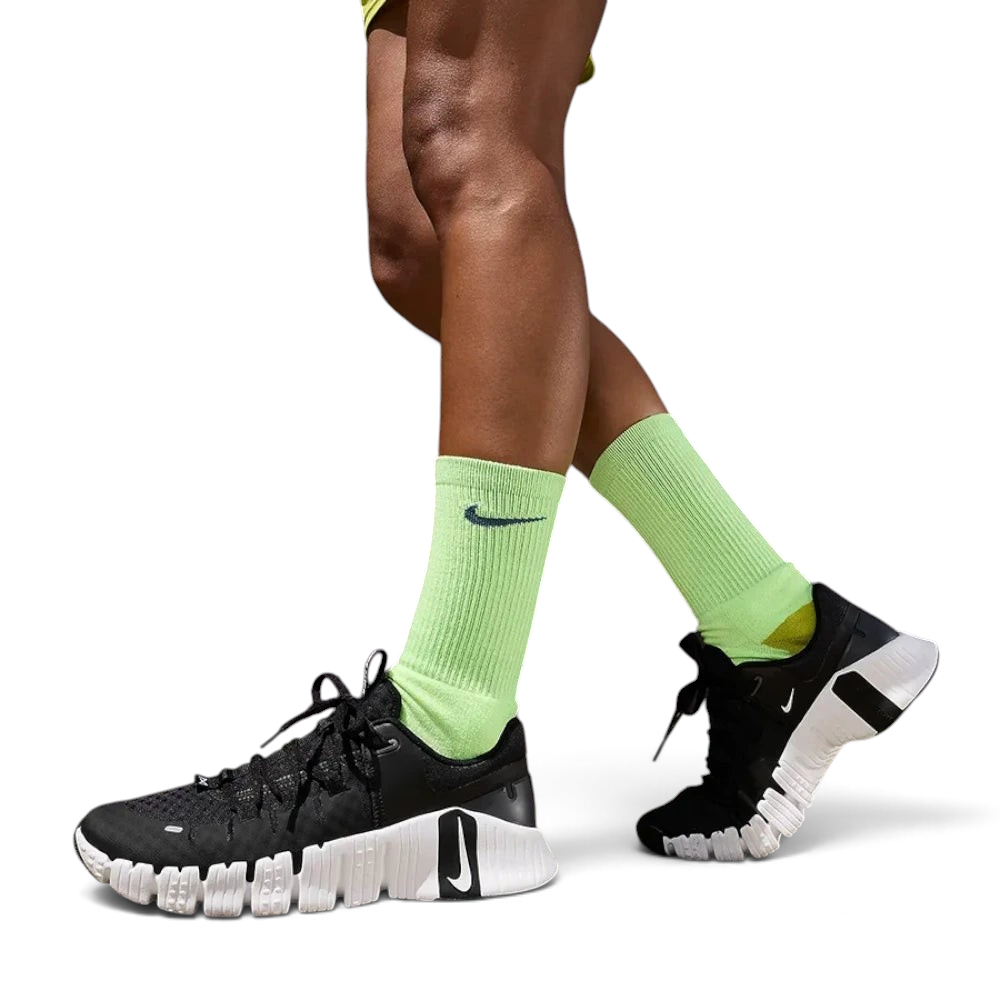 Person wearing black Nike sneakers and bright green socks against a dark textured wall.