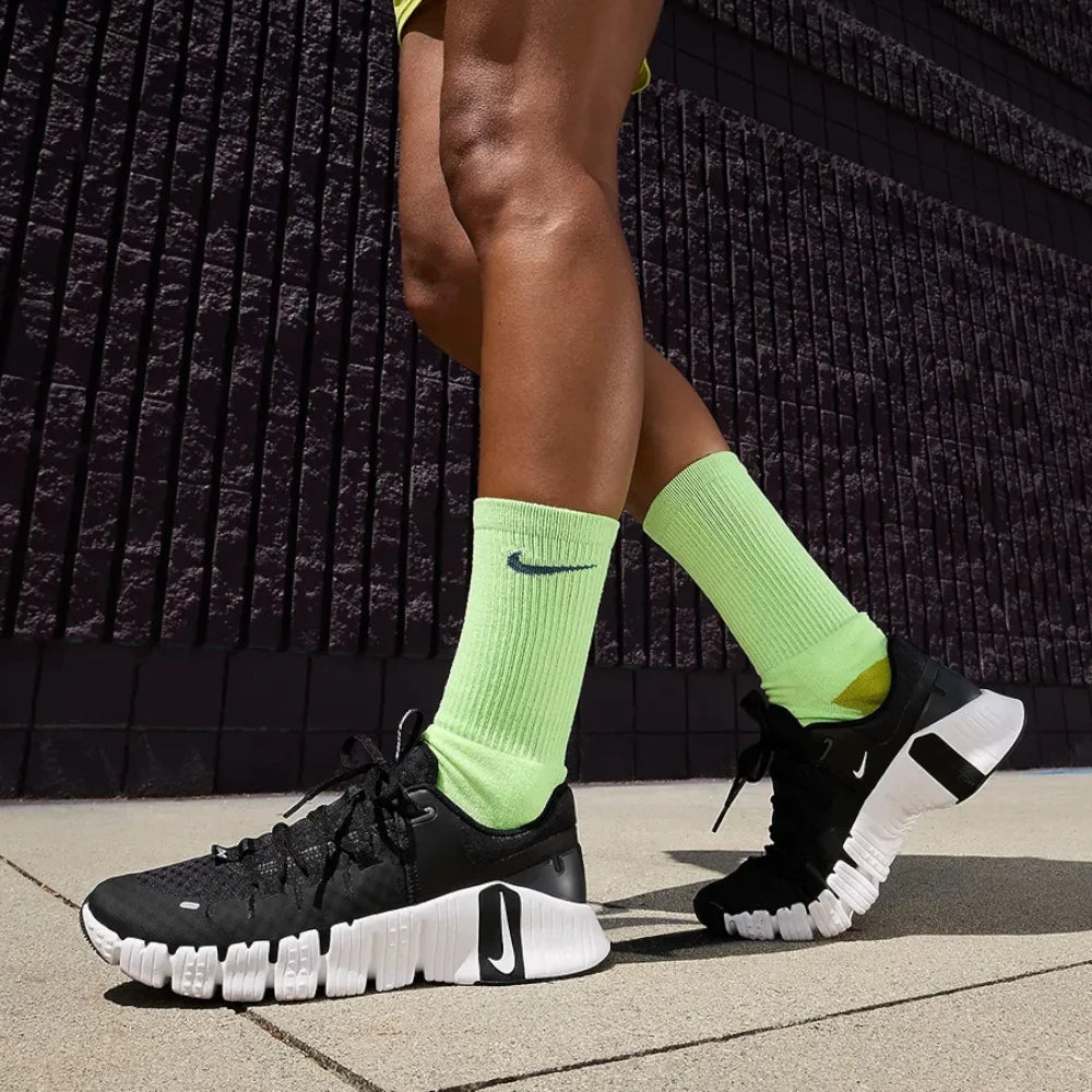 Person wearing black Nike sneakers and bright green socks against a dark textured wall.