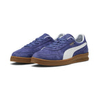 Forward three-quarter angle showcasing both shoes side by side, highlighting the low-slung indoor court stance, perforated suede toe boxes, tonal blue laces, white leather Formstrips, and classic gum cupsole tooling.