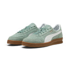 Forward three-quarter angle showcasing both shoes side by side, highlighting the low-slung indoor court stance, perforated suede toe box, tonal green laces, and classic gum cupsole tooling.