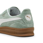 Close-up rear angle focusing on the Green Moon suede heel counter, white textured leather heel moustache tab stamped with a gilded metallic PUMA Cat logo, and the sculpted gum rubber heel bumper.