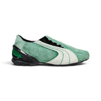 Displays the lateral profile showing the mossy-green hairy cow suede upper, double-piped white suede Formstrip, black-cased external heel counter with emerald green insert windows, concealed asymmetric lace shroud, and low-slung black turf-cleat rubber sole.