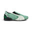 Displays the lateral profile showing the mossy-green hairy cow suede upper, double-piped white suede Formstrip, black-cased external heel counter with emerald green insert windows, concealed asymmetric lace shroud, and low-slung black turf-cleat rubber sole.