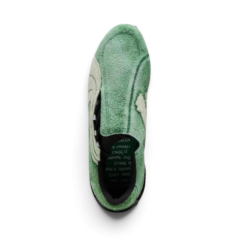 Direct overhead look highlighting the asymmetric rounded toe shape, moss-green hairy suede shroud with exposed lacing throat, and dark interior sockliner printed with handwritten collaborative KidSuper notes.