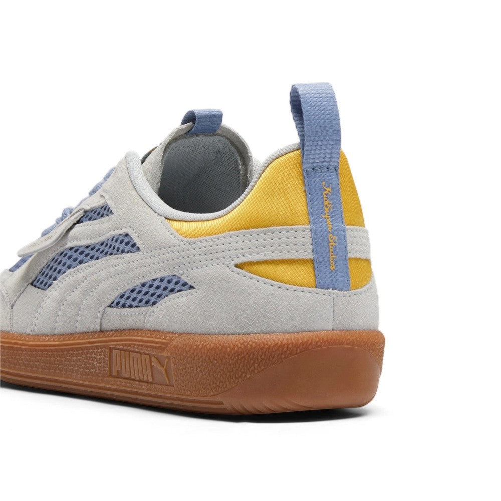Close-up rear angle focusing on the mustard yellow satin collar accent, grey suede heel counter, and light blue vertical heel pull tab embroidered with orange "KidSuper Studios" branding above the gum rubber sole bumper.