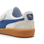 Close-up rear angle focusing on the Vapor Gray suede heel counter, royal blue suede heel moustache tab stamped with a gilded metallic PUMA Cat logo, soft white collar lining, and textured gum cupsole base.