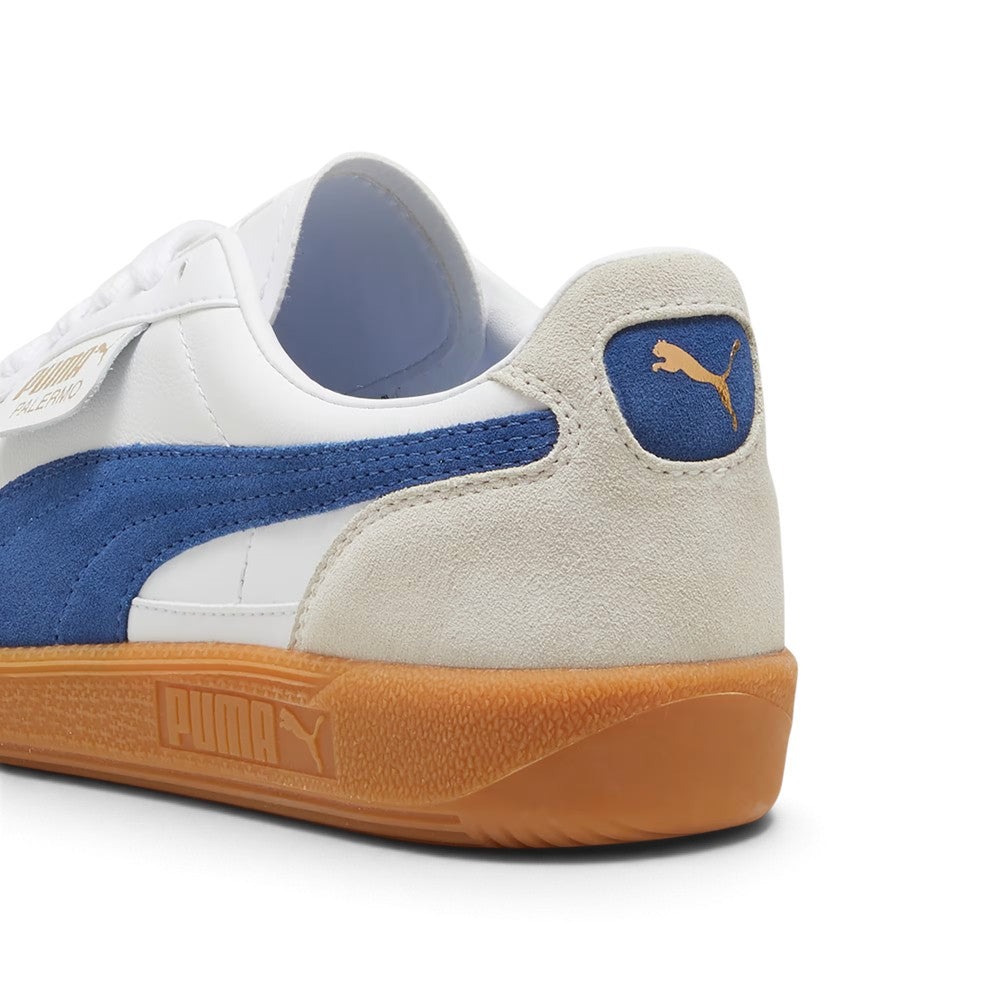 Close-up rear angle focusing on the Vapor Gray suede heel counter, royal blue suede heel moustache tab stamped with a gilded metallic PUMA Cat logo, soft white collar lining, and textured gum cupsole base.