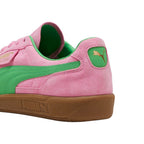 Close-up rear angle focusing on the Pink Delight suede heel counter, bright PUMA Green smooth leather heel moustache tab stamped with a gilded metallic PUMA Cat logo, soft green collar lining, and textured gum cupsole base.
