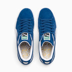 Direct overhead look at both shoes, displaying the Olympian Blue suede toe boxes, flat blue laces through punched suede eyestays, white-and-green woven PUMA tongue tags, and white footbeds stamped with an intricate gold foil repeating PUMA pattern.