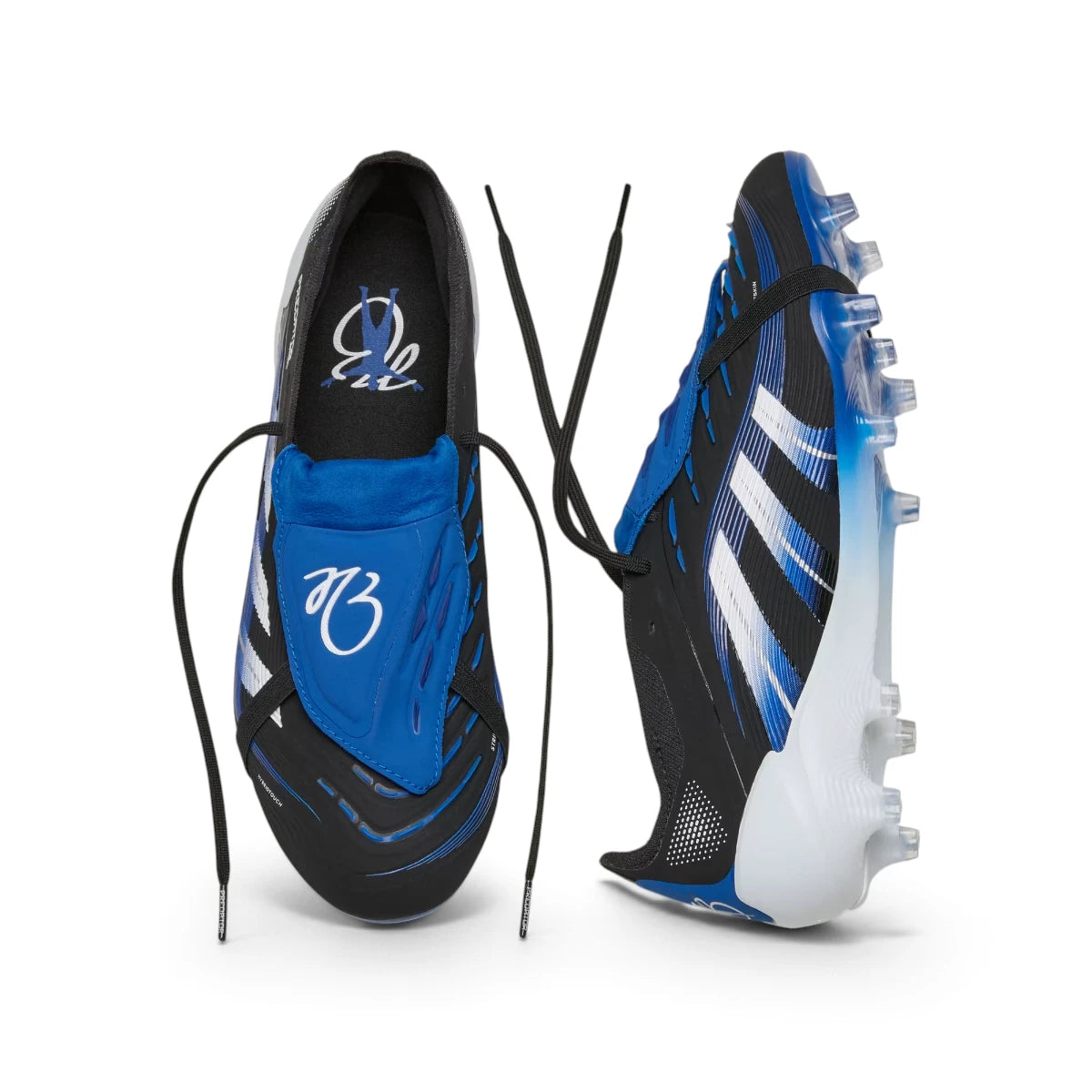 Overhead layout of the paired boots, displaying the black laces, the vibrant blue fold-over tongues featuring Jude Bellingham's signature "JB" branding, and the branded insoles.