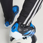 Close-up shot of a player's feet wearing the signature boots, focusing on the blue heel counter adorned with Jude Bellingham's iconic silhouette celebration graphic and the specialized firm ground studs.