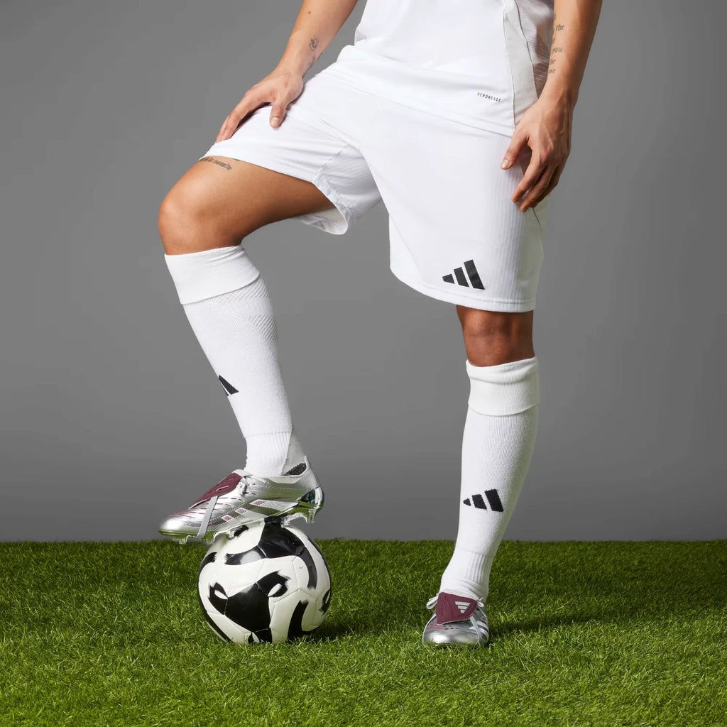 Player wearing the silver and burgundy Predator Elite boots while resting a foot atop a football on an artificial turf pitch.