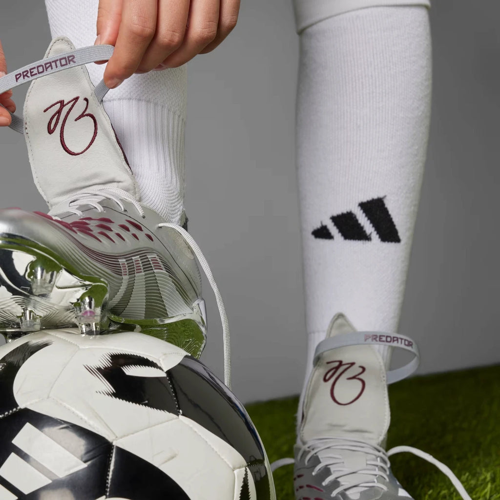 Detail shot of a player adjusting the elastic retention strap over the unfolded burgundy tongue, revealing the "PREDATOR" branding on the strap.