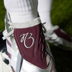 Macro focus on the rich burgundy fold-over tongue highlighting the embroidered silver signature "JB" logo and integrated strike elements.