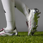 Close-up action perspective capturing a player running on grass, showcasing the reflective chrome outsole finish and silver upper profile.