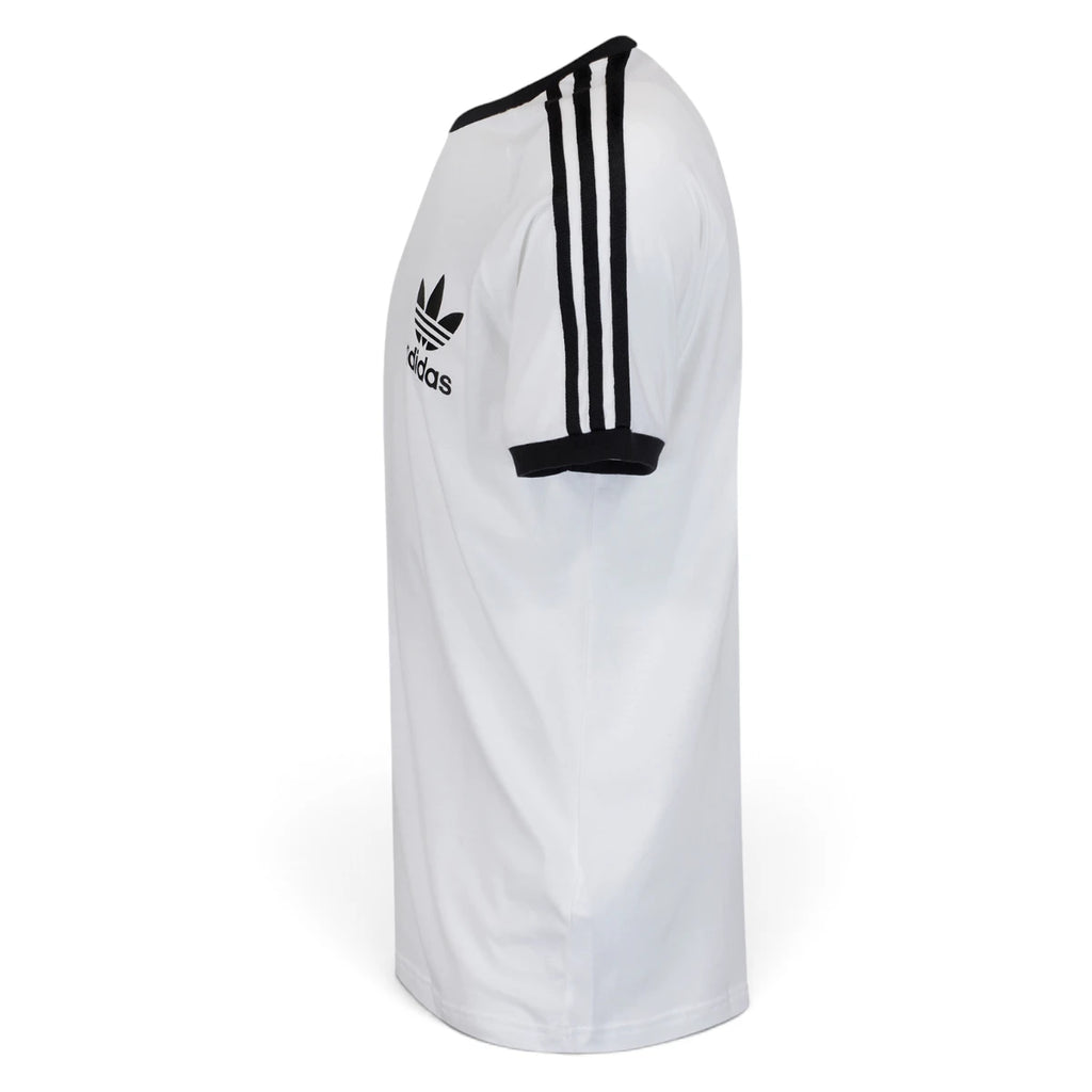 Side Profile Image: Studio lateral shot of the adidas California t-shirt in white and black, highlighting the raglan shoulder seam, black sleeve cuff, and continuous triple-stripe tape running down the arm.   