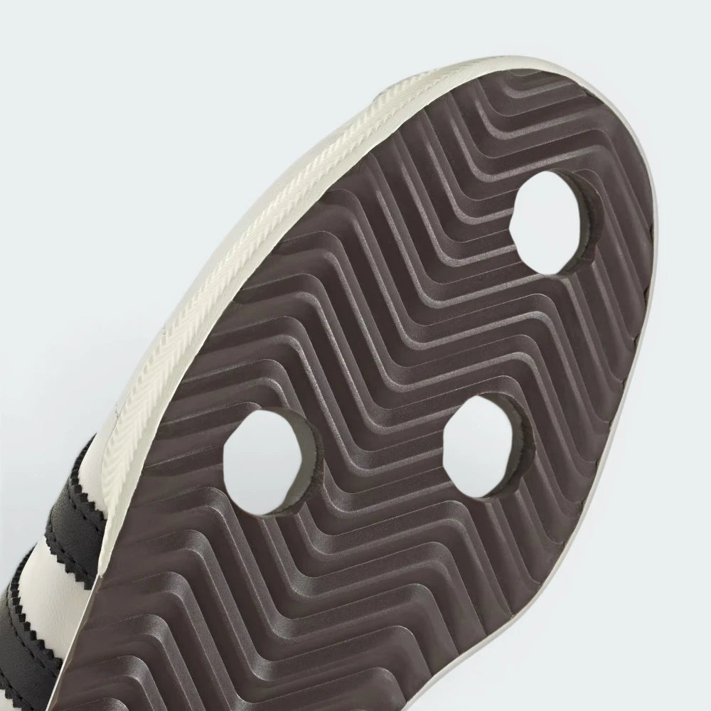 Close-up of a shoe sole with a textured pattern and three white hexagonal studs on a light gray background.