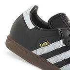 Detailed close-up angle capturing the gold foil "SAMBA" lettering, stitched leather panels, and the textured edge of the gum midsole.