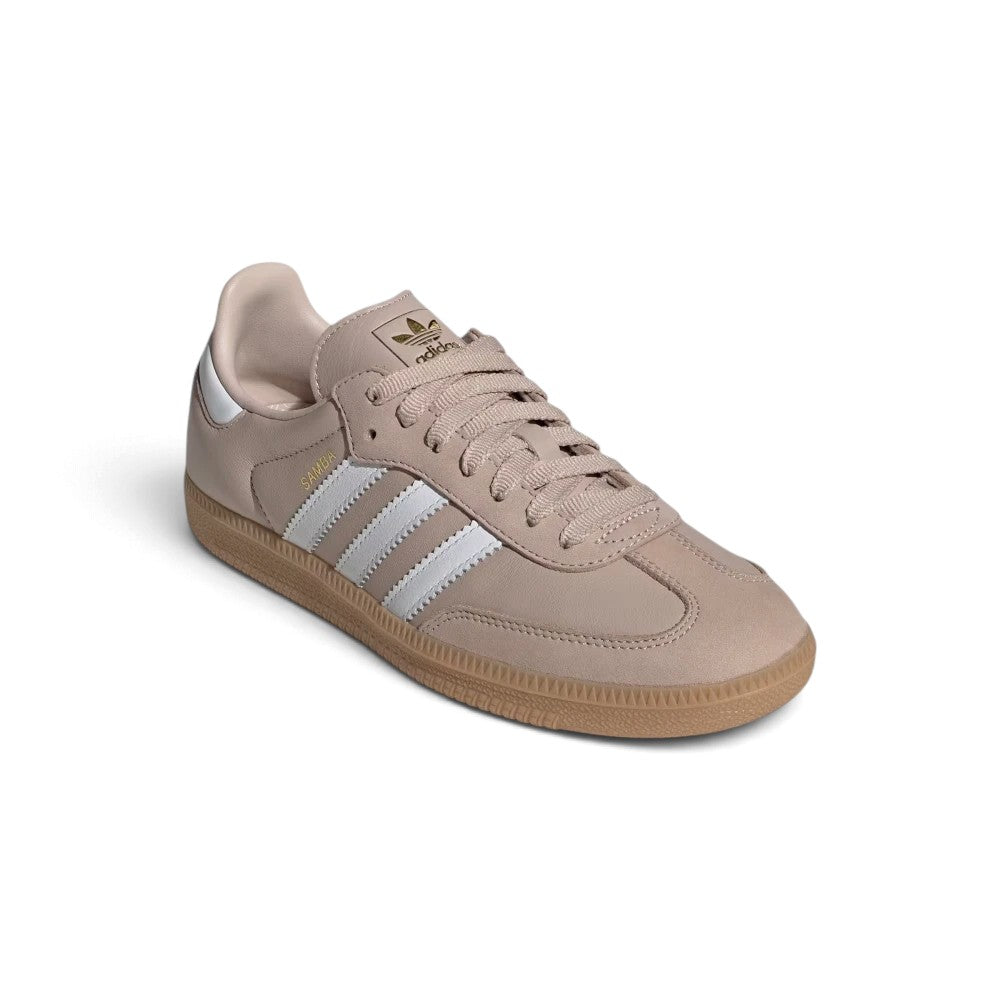 Forward three-quarter angle showcasing the trainer propped up, highlighting the low-slung terrace stance, supple leather texture, flat taupe laces, and timeless taupe-and-white contrast.