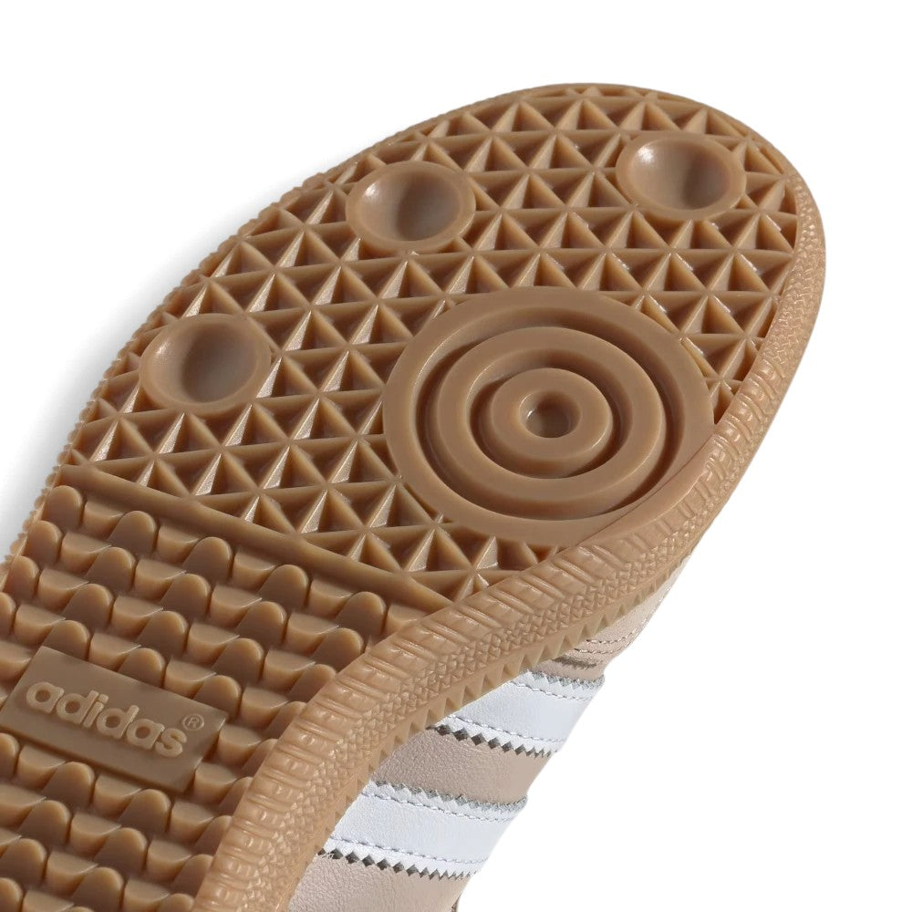 Close-up of the textured brown Adidas outsole showing the circular central tread and the embossed Adidas logo, with a white striped shoe upper partially visible underneath on a white background.