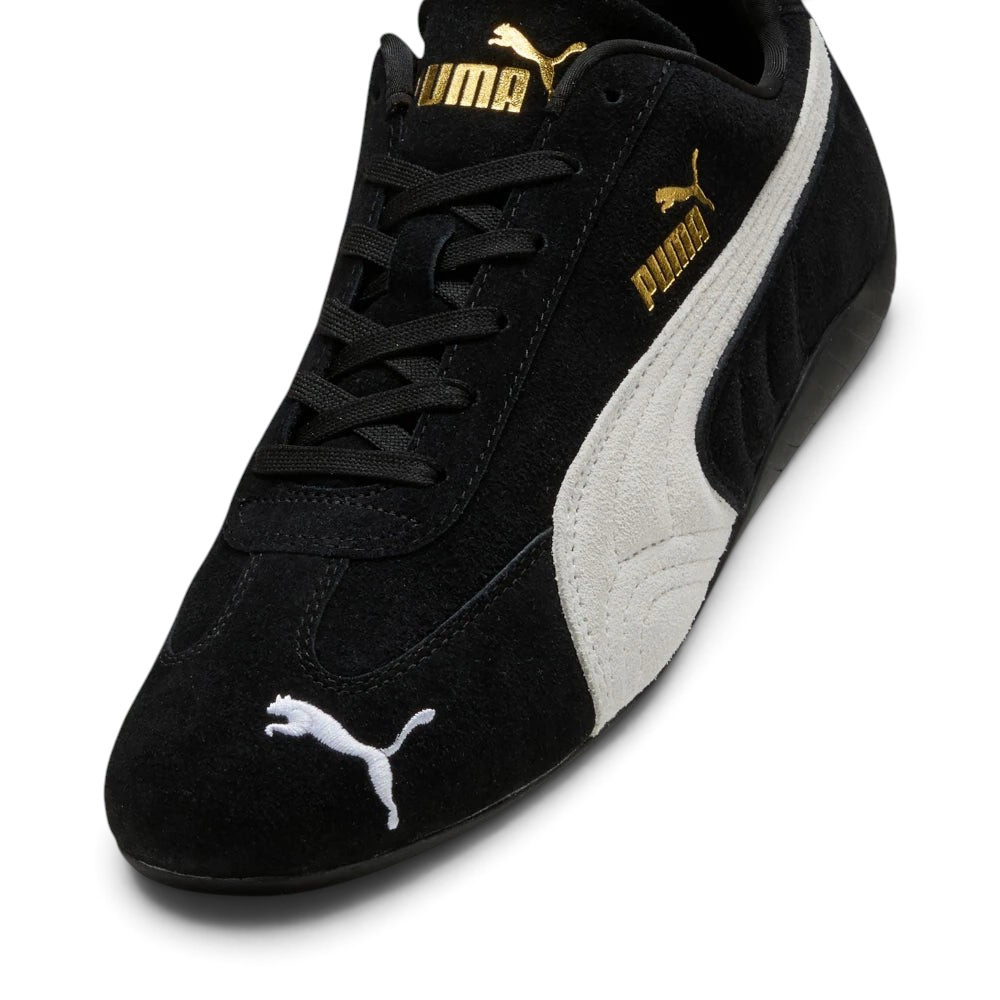 Details the premium precision of the white embroidered Puma Cat logo sitting on the black suede toe box, highlighting the soft nap of the suede, the clean eyelet stitching, and the gold foil Puma branding on the side.