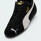 Details the premium precision of the white embroidered Puma Cat logo sitting on the black suede toe box, highlighting the soft nap of the suede, the clean eyelet stitching, and the gold foil Puma branding on the side.
