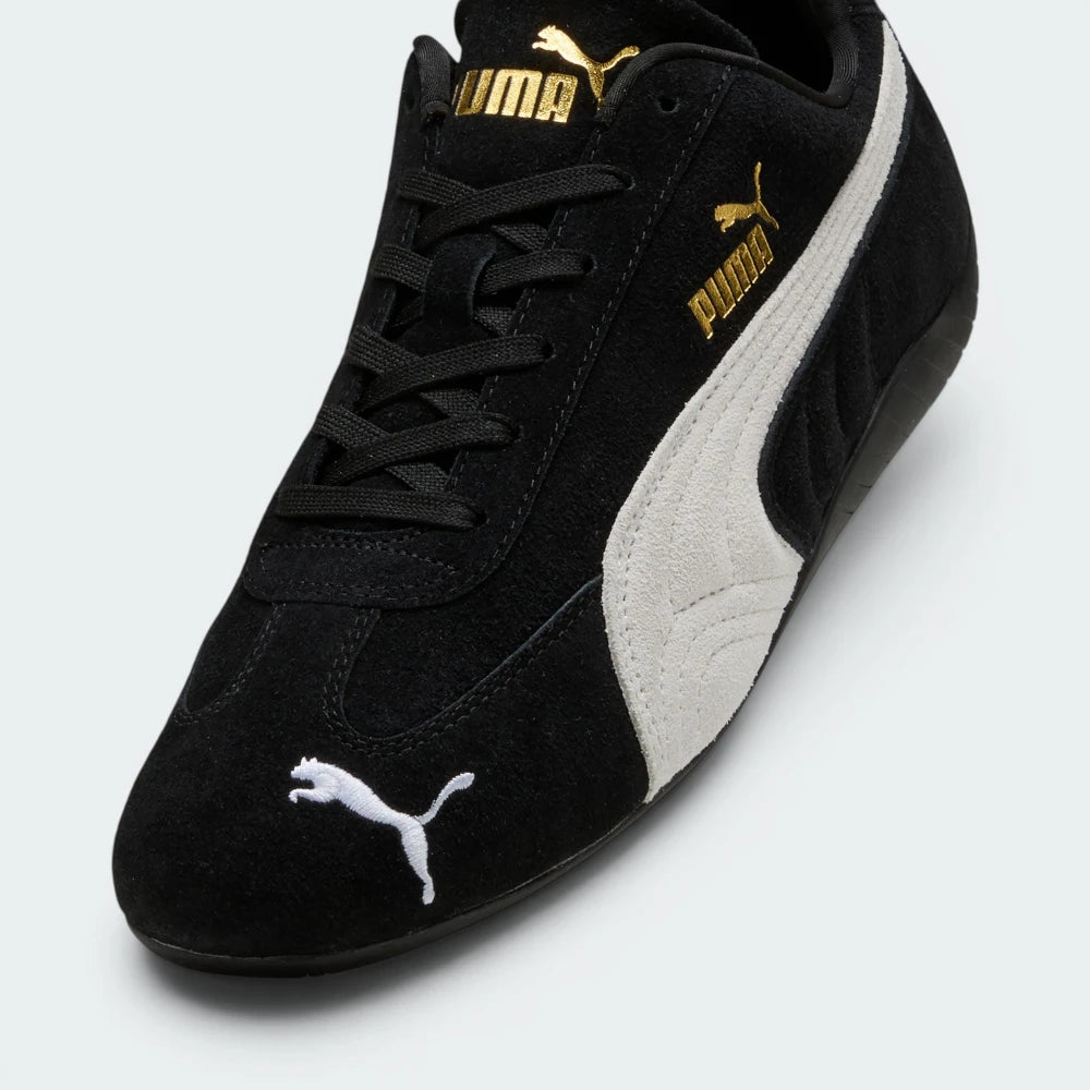 Details the premium precision of the white embroidered Puma Cat logo sitting on the black suede toe box, highlighting the soft nap of the suede, the clean eyelet stitching, and the gold foil Puma branding on the side.
