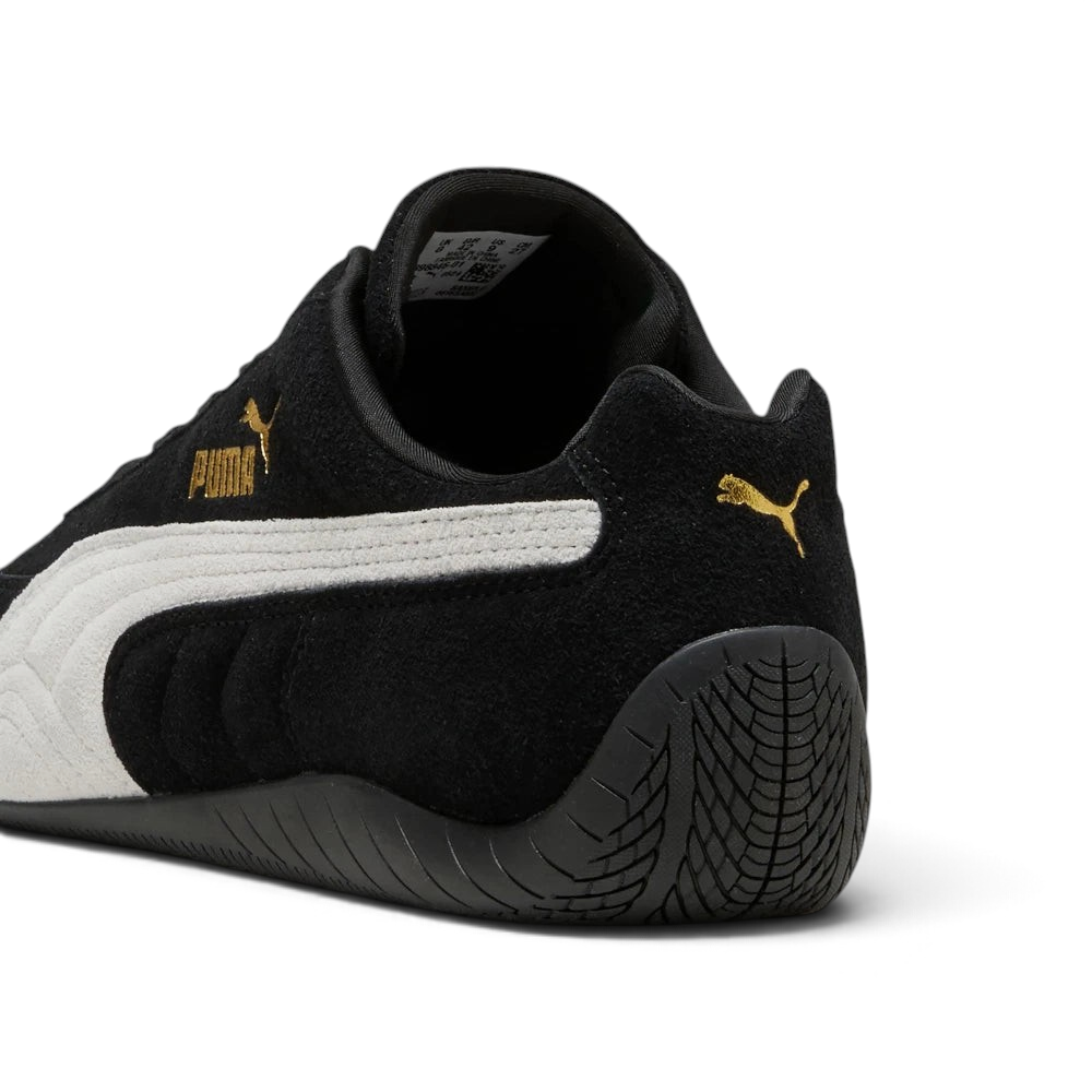 Focuses on the rounded driver's heel design, showcasing the tire-tread textured black rubber wrapping up the rear spine, finished with a small metallic gold Puma Cat logo.