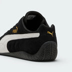 Focuses on the rounded driver's heel design, showcasing the tire-tread textured black rubber wrapping up the rear spine, finished with a small metallic gold Puma Cat logo.