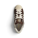 Overhead view looking down at the laced brown trainers, displaying the cream flat laces, gold foil branded tongue label, and clean interior lining.