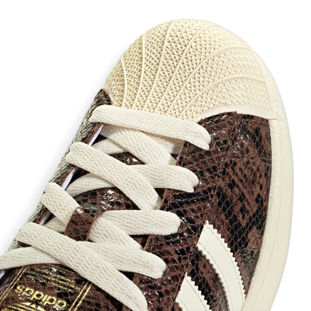 Macro focus on the textured rubber shell toe cap, crossover lacing, and the fine reptilian pattern of the brown leather.