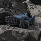 Blue athletic shoes with black soles on a rocky surface