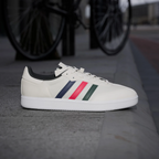 White sneaker with colorful stripes on a concrete surface with a blurred bicycle in the background