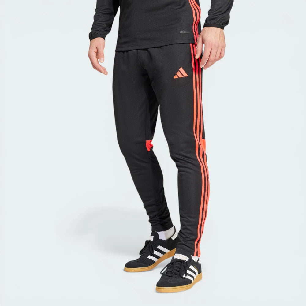 Side profile of the Black and Lucid Red Tiro 25 pants, highlighting the vibrant red 3-Stripes and the tapered leg silhouette.