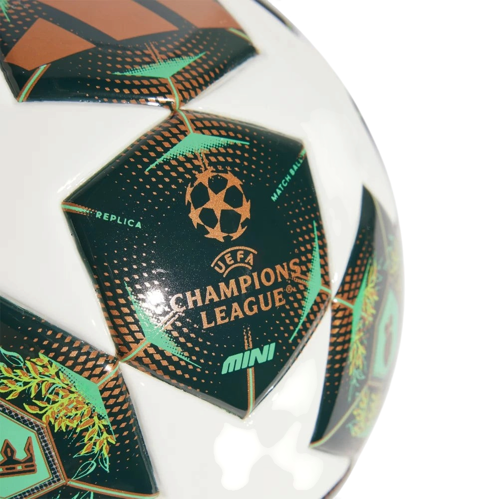 Details a tight close-up view of a single panel, showcasing the high-gloss smooth TPU texture, the printed bronze UEFA Champions League starball emblem and text branding, and the clean "MINI" and "REPLICA" typography.