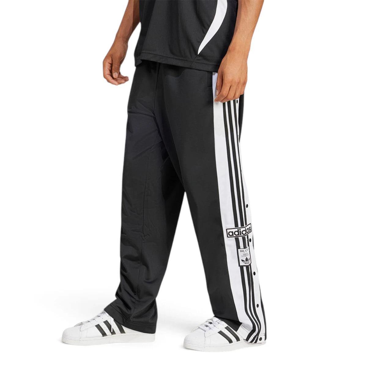Studio side profile view of a male model wearing the adidas Originals Adibreak Pants in black, highlighting the regular fit, classic white 3-Stripes, functional snap-button side panels, and retro Adibreak leg patch. Main image
