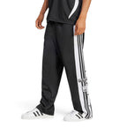 Studio side profile view of a male model wearing the adidas Originals Adibreak Pants in black, highlighting the regular fit, classic white 3-Stripes, functional snap-button side panels, and retro Adibreak leg patch.