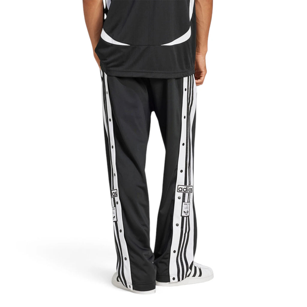 Studio rear-facing perspective showcasing the clean black rear tricot panels, straight-leg drape, and the continuation of the snap-button side stripes down to the footwear.