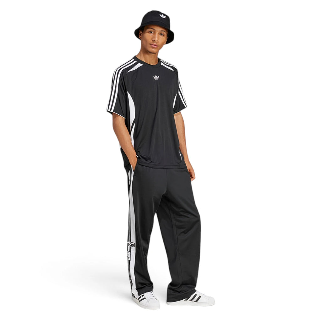 Full-length studio shot of a male model wearing the complete black Adibreak track look paired with a bucket hat and white shell-toe trainers, demonstrating its relaxed, everyday styling.