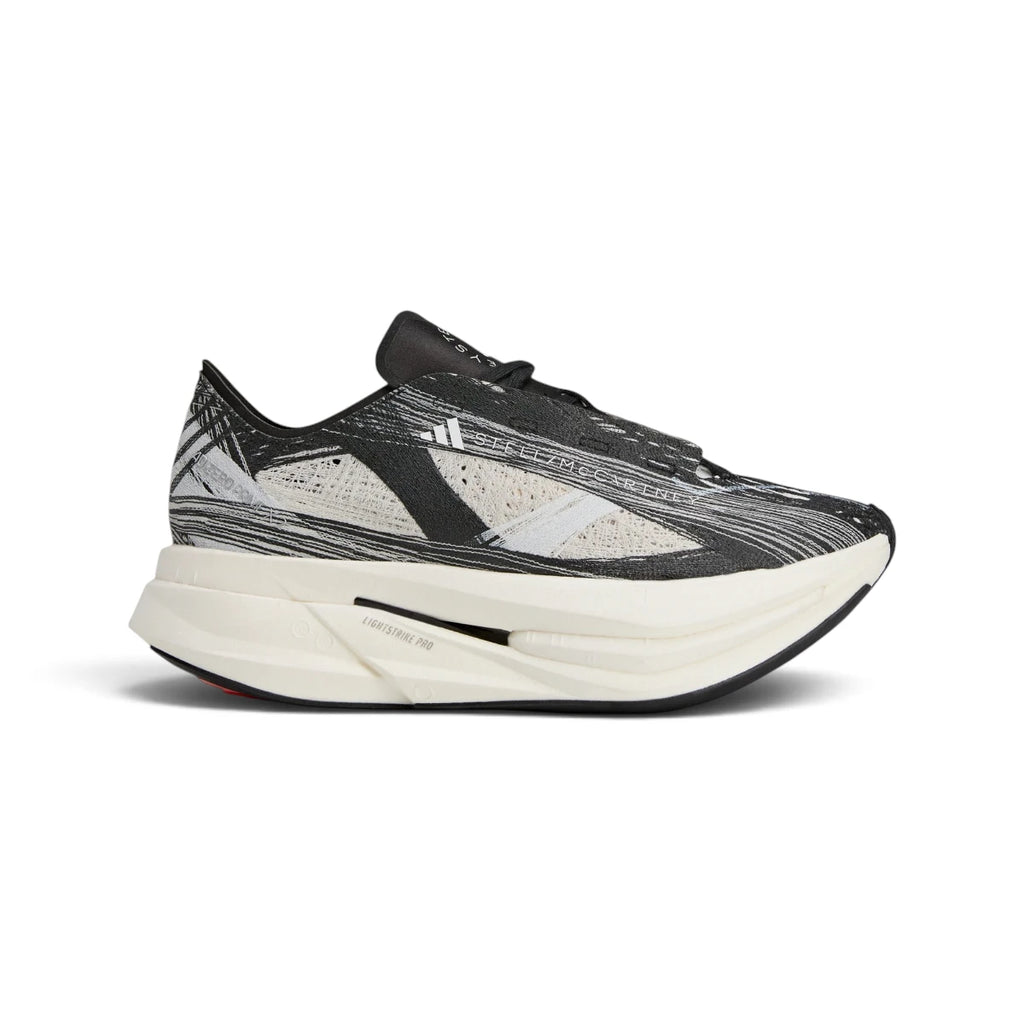 Studio side-profile shot of the adidas by Stella McCartney Prime x 2.0 STRUNG shoes in Cloud White, Grey One, and Core Black, highlighting the data-mapped STRUNG upper, stacked white midsole, Lightstrike Pro branding, and Continental rubber outsole.