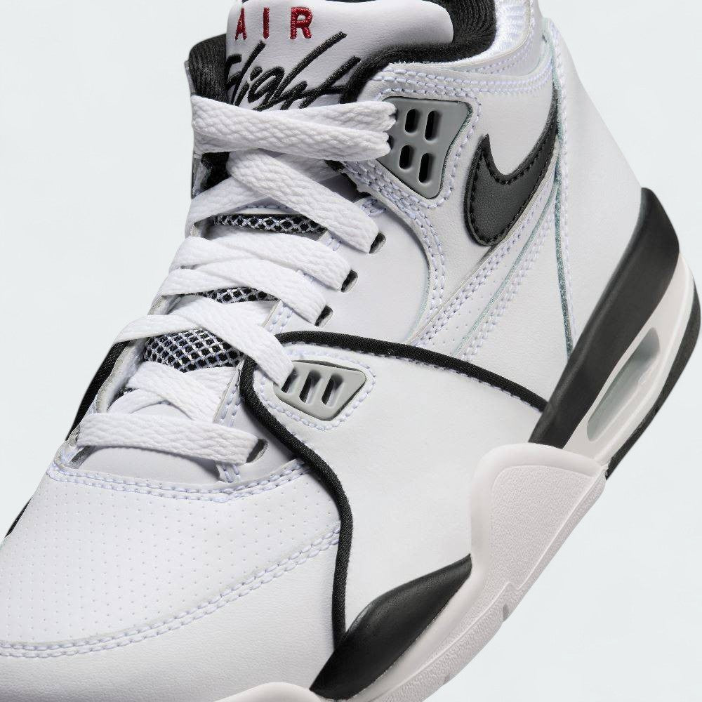 Close-up zoom on the front of the Nike Air Flight 89 Juniors' white trainers, showing the perforated toe box, lacing system, and texture of the leather upper.