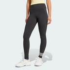 Front three-quarter view of a model wearing the black adidas Neuclassics leggings paired with white trainers, showing the high-waisted fit, full-length leg coverage, and three horizontal white stripes wrapping around the left lower shin.